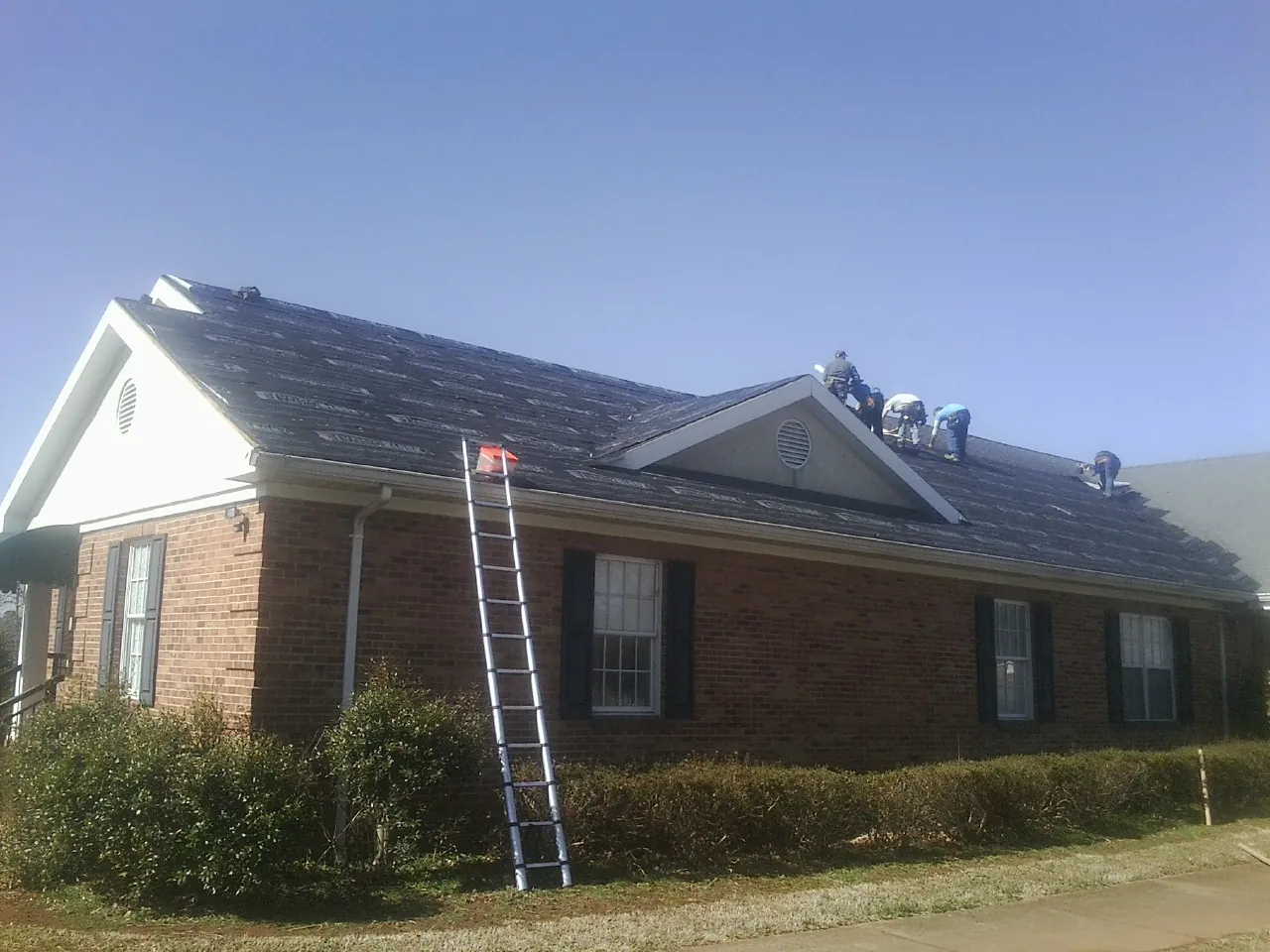 Crew tearing shingles off a brick ranch roof with a ladder set — Metal Roof Repair work by our crew in Tell City