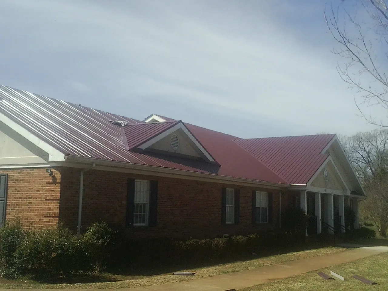 Red metal roof with gabled entries on a long brick building, from a Hail Damage Roof Repair job in Tell City