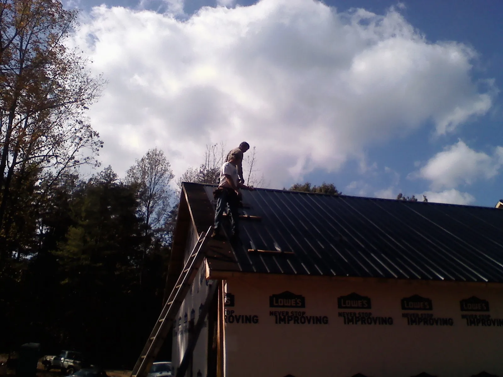 Roofer fastening dark metal panels high against a cloudy sky, from a Roof Inspection job in Tell City