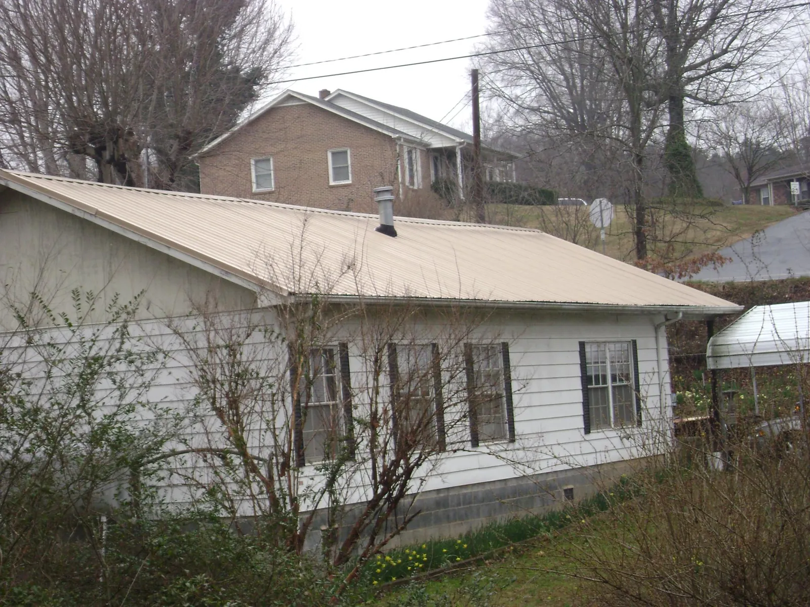 Tan metal roof on a white sided house set into a hillside — Commercial Roofing by Roofing Brothers in Tell City