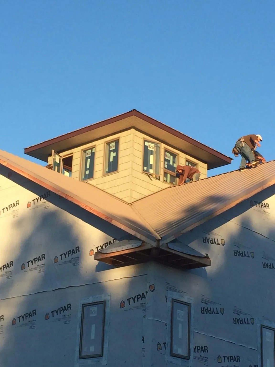 Roofers working around a rooftop cupola on a new metal roof at sunset in Tell City